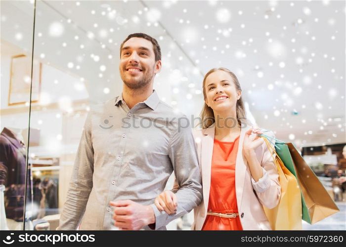 sale, consumerism and people concept - happy young couple with shopping bags walking in mall with snow effect