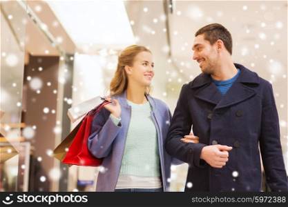 sale, consumerism and people concept - happy young couple with shopping bags walking and talking in mall with snow effect