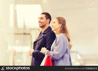 sale, consumerism and people concept - happy young couple with shopping bags looking to shopwindow in mall