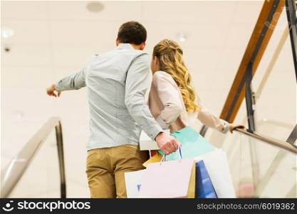 sale, consumerism and people concept - happy young couple with shopping bags raising up by escalator and pointing finger in mall