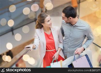 sale, consumerism and people concept - happy young couple with shopping bags rising on escalator and talking in mall. happy young couple with shopping bags in mall