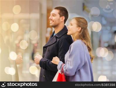 sale, consumerism and people concept - happy young couple with shopping bags looking to shopwindow in mall. happy young couple with shopping bags in mall