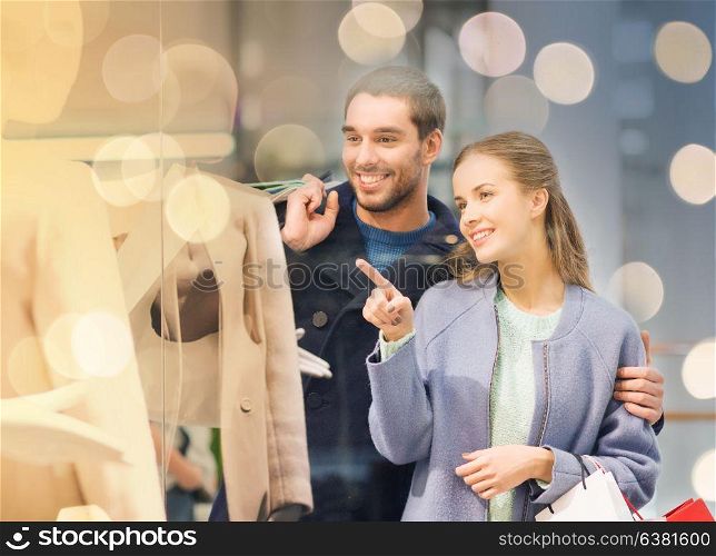 sale, consumerism and people concept - happy young couple with shopping bags pointing finger to shop window in mall. happy young couple with shopping bags in mall