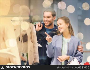 sale, consumerism and people concept - happy young couple with shopping bags pointing finger to shop window in mall. happy young couple with shopping bags in mall