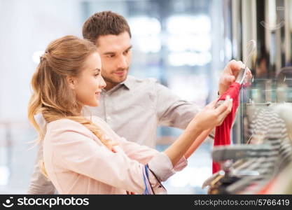 sale, consumerism and people concept - happy young couple with shopping bags choosing dress in mall