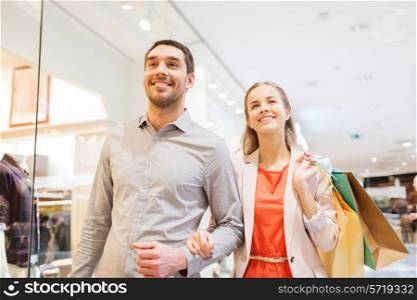sale, consumerism and people concept - happy young couple with shopping bags walking in mall