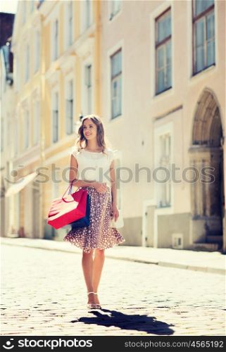 sale, consumerism and people concept - happy young woman with shopping bags walking along city street