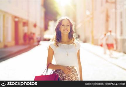 sale, consumerism and people concept - happy young woman with shopping bags walking along city street. happy woman with shopping bags walking in city