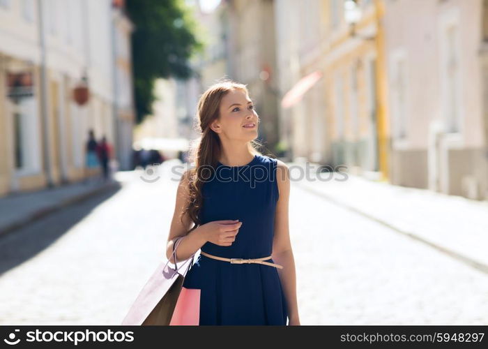 sale, consumerism and people concept - happy young woman with shopping bags walking along city street