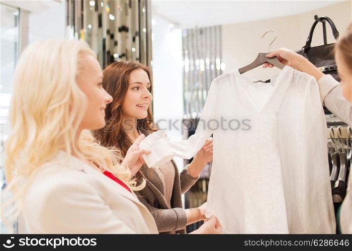 sale, consumerism and people concept - happy young women choosing clothes in mall