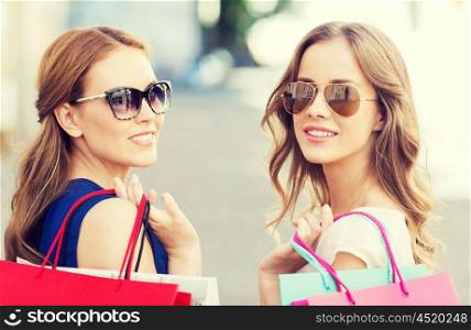 sale, consumerism and people concept - happy young women in sunglasses with shopping bags on city street
