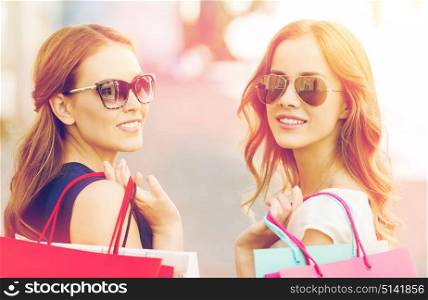 sale, consumerism and people concept - happy young women in sunglasses with shopping bags on city street. happy young women with shopping bags in city