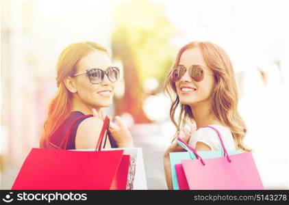 sale, consumerism and people concept - happy young women in sunglasses with shopping bags on city street. happy young women with shopping bags in city
