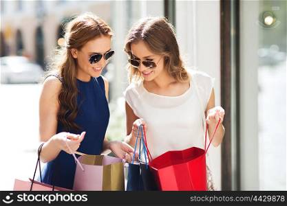 sale, consumerism and people concept - happy young women looking into shopping bags at shop window in city