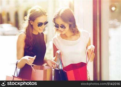 sale, consumerism and people concept - happy young women looking into shopping bags at shop window in city. happy women with shopping bags in city