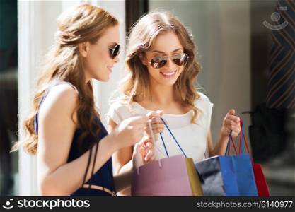 sale, consumerism and people concept - happy young women looking into shopping bags at shop window in city