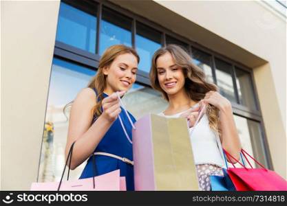 sale, consumerism and people concept - happy young women looking into shopping bags at storefront. happy women with shopping bags at storefront