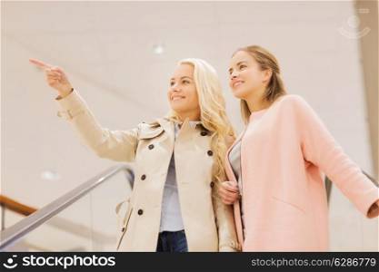 sale, consumerism and people concept - happy young women pointing finger on escalator in mall