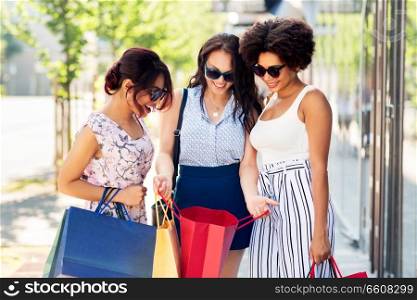 sale, consumerism and people concept - happy young women showing shopping bags on city street. happy women showing shopping bags in city