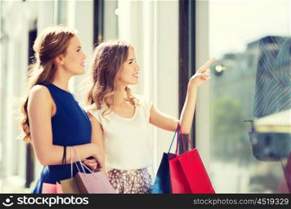 sale, consumerism and people concept - happy young women with shopping bags pointing finger to shop window in city