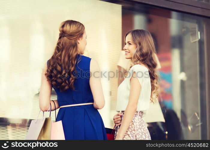 sale, consumerism and people concept - happy young women with shopping bags talking at to shop window in city from back