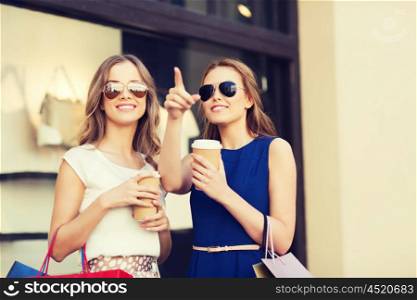 sale, consumerism and people concept - happy young women with shopping bags and coffee paper cup pointing finger at shop window in city