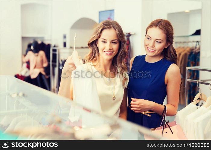 sale, consumerism and people concept - happy young women with shopping bags choosing clothes at clothing shop