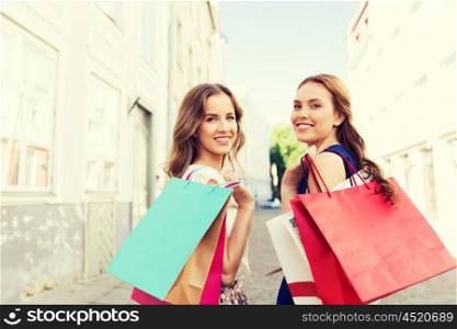 sale, consumerism and people concept - happy young women with shopping bags walking along city street and looking back