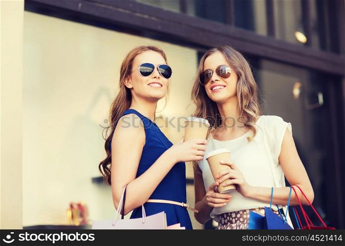 sale, consumerism and people concept - happy young women with shopping bags and coffee paper cups at shop window in city