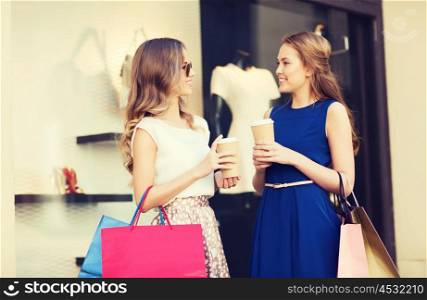 sale, consumerism and people concept - happy young women with shopping bags and coffee paper cups talking at shop window in city