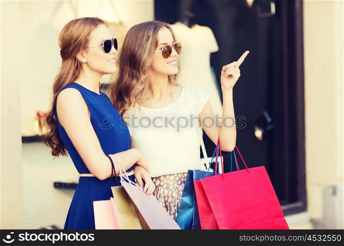 sale, consumerism and people concept - happy young women with shopping bags pointing finger at shop window in city