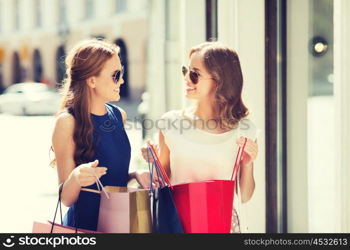 sale, consumerism and people concept - happy young women with shopping bags talking at shop window in city