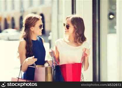 sale, consumerism and people concept - happy young women with shopping bags talking at shop window in city