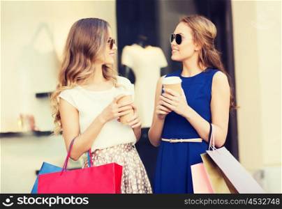 sale, consumerism and people concept - happy young women with shopping bags and coffee paper cups talking at shop window in city