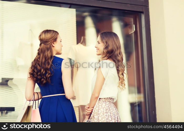 sale, consumerism and people concept - happy young women with shopping bags talking at to shop window in city from back