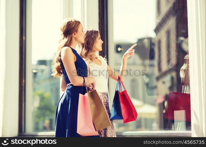 sale, consumerism and people concept - happy young women with shopping bags pointing finger to shop window in city