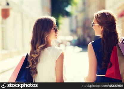 sale, consumerism and people concept - happy young women with shopping bags walking along city street and talking