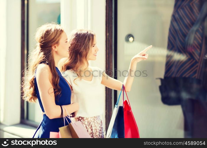 sale, consumerism and people concept - happy young women with shopping bags pointing finger to shop window in city