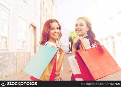 sale, consumerism and people concept - happy young women with shopping bags walking along city street and looking back. happy women with shopping bags walking in city