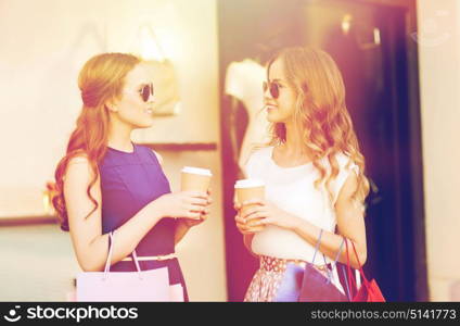 sale, consumerism and people concept - happy young women with shopping bags and coffee paper cups talking at shop window in city. young women with shopping bags and coffee at shop