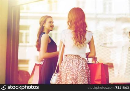 sale, consumerism and people concept - happy young women with shopping bags talking at to shop window in city from back. happy women with shopping bags at shop window