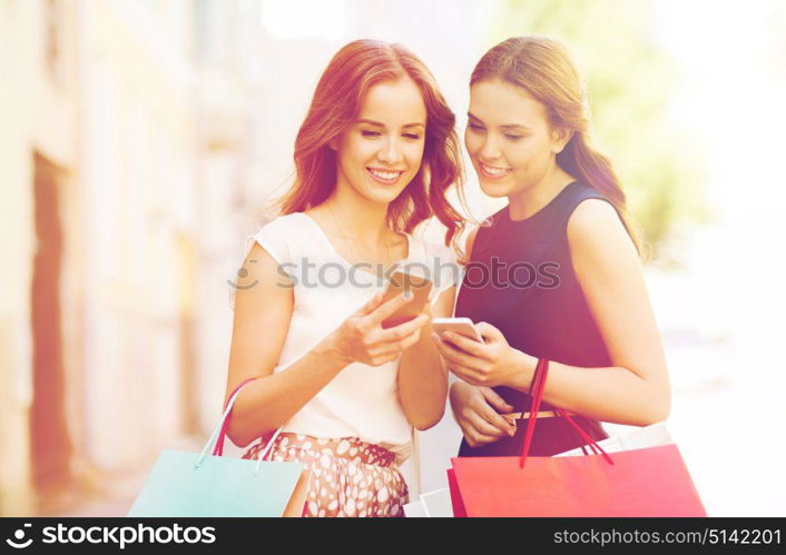 sale, consumerism and people concept - happy young women with shopping bags and smartphone on city street. happy women with shopping bags and smartphone