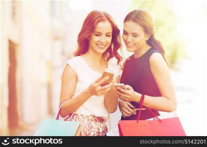 sale, consumerism and people concept - happy young women with shopping bags and smartphone on city street. happy women with shopping bags and smartphone