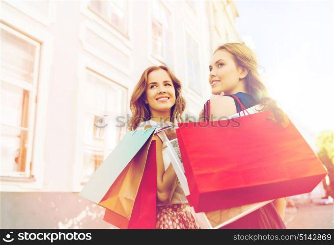 sale, consumerism and people concept - happy young women with shopping bags walking along city street and looking back. happy women with shopping bags walking in city