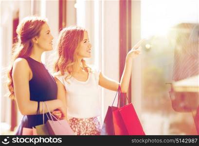 sale, consumerism and people concept - happy young women with shopping bags pointing finger to shop window in city. happy women with shopping bags at shop window