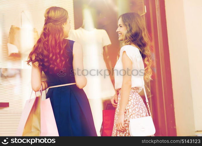 sale, consumerism and people concept - happy young women with shopping bags talking at to shop window in city from back. happy women with shopping bags at shop window