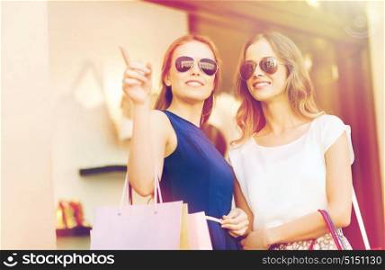 sale, consumerism and people concept - happy young women with shopping bags pointing finger at shop window in city. happy young women with shopping bags in mall