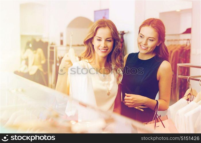 sale, consumerism and people concept - happy young women with shopping bags choosing clothes at clothing shop. happy women with shopping bags at clothing shop