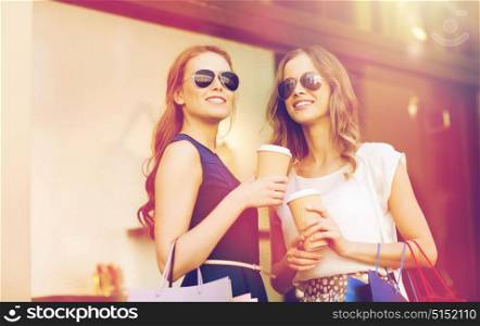 sale, consumerism and people concept - happy young women with shopping bags and coffee paper cups at shop window in city. young women with shopping bags and coffee at shop