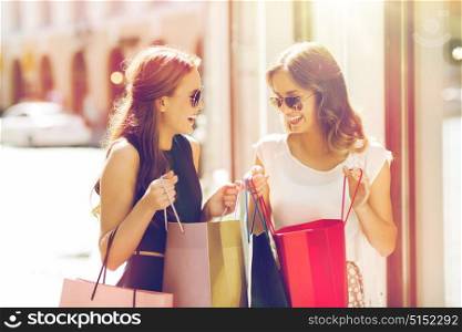 sale, consumerism and people concept - happy young women with shopping bags talking at shop window in city. happy women with shopping bags in city
